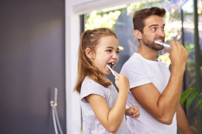 A man and young girl brushing their teeth.